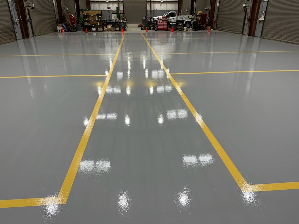 A photo of a seamless, glossy and reflective industrial floor made of resinous epoxy material. The floor is evenly coated with the epoxy material and appears to be durable and long-lasting